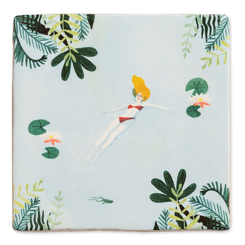 StoryTile Me-time. Op deze decoratietegel staat een vrouw die drijvend in het water lekker ontspant. Ze drijft tussen de waterlelies in een rode bikini. 