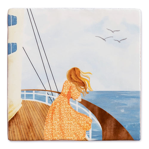 StoryTile Zicht op de horizon. Mooie ambachtelijk gebakken tegel met daarop een afbeelding van een vrouw met lange oranje haren in een lange oranje jurk die op een schip staat en over de zee staart. 