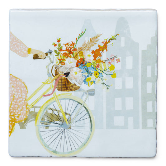 StoryTile Vroljikheid in een fietsmand. Vrolijke tegel met iemand op een fiets met een fietsmand vol kleurige bloemen. Degene op de fiets ziet je half en de bloemen trekken de aandacht. 