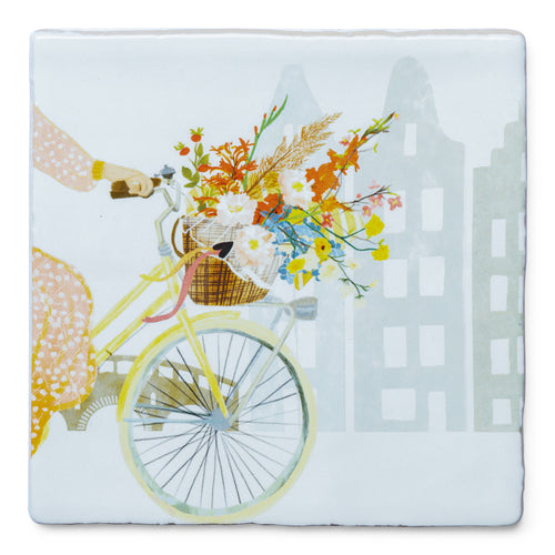 StoryTile Vroljikheid in een fietsmand. Vrolijke tegel met iemand op een fiets met een fietsmand vol kleurige bloemen. Degene op de fiets ziet je half en de bloemen trekken de aandacht. 